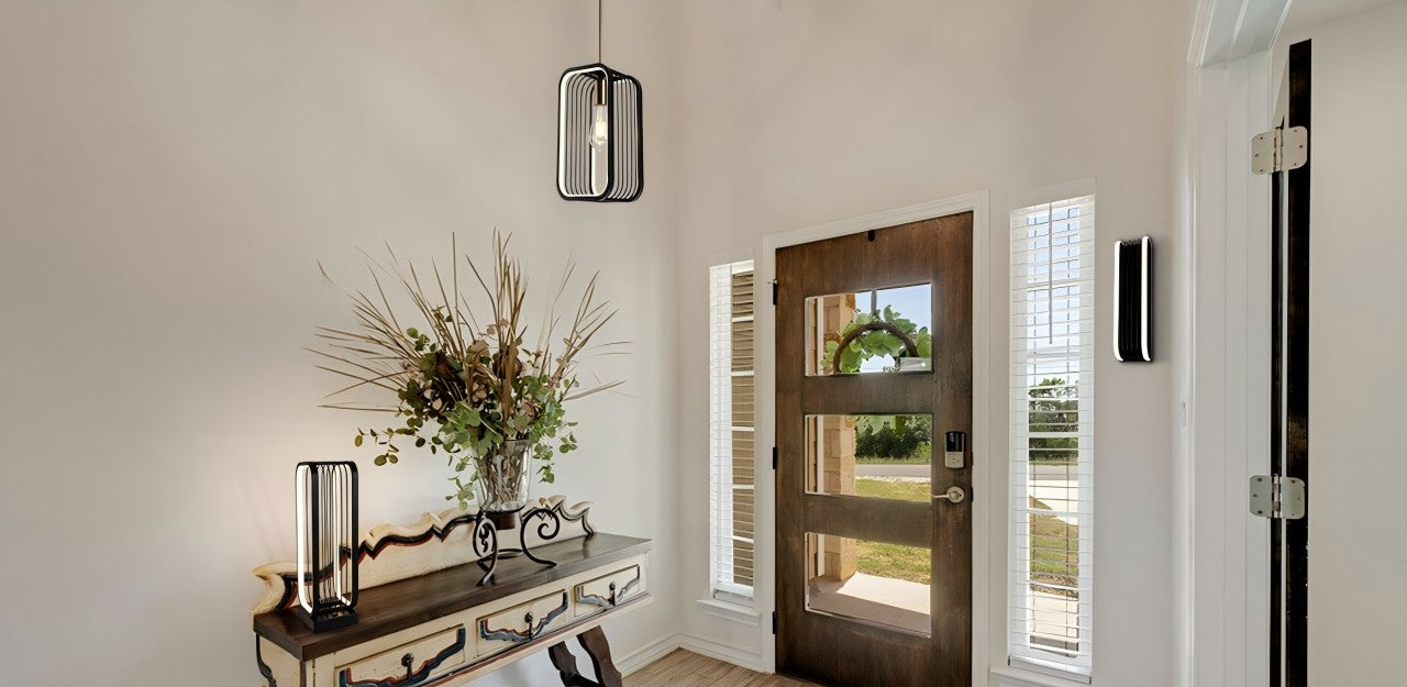 In foyer, 3 lamps: sq. pendant (simple, modern) above, unique table lamp (strong lines) on table, simple wall lamp on wall. Complement decor, make warm, stylish vibe.